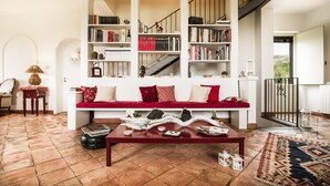 A living room with a red sofa, a wooden coffee table, and bookshelves filled with books. - Nake Residenza Artistica (Sant'Alfio)