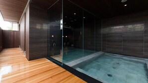 A modern spa with a glass-enclosed hot tub, wooden flooring, and dark wooden walls. - Hotel Kikyou (Kaga)