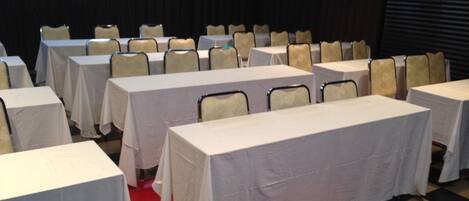 A conference room with multiple tables and chairs, arranged in rows.
