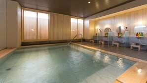 A swimming pool with a wooden deck, a changing room area with mirrors and sinks, and a wooden wall with a window. - Hotel Kikyou (Kaga)