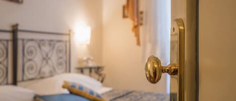 A room with a bed, a nightstand, a lamp, and a door with a brass handle.