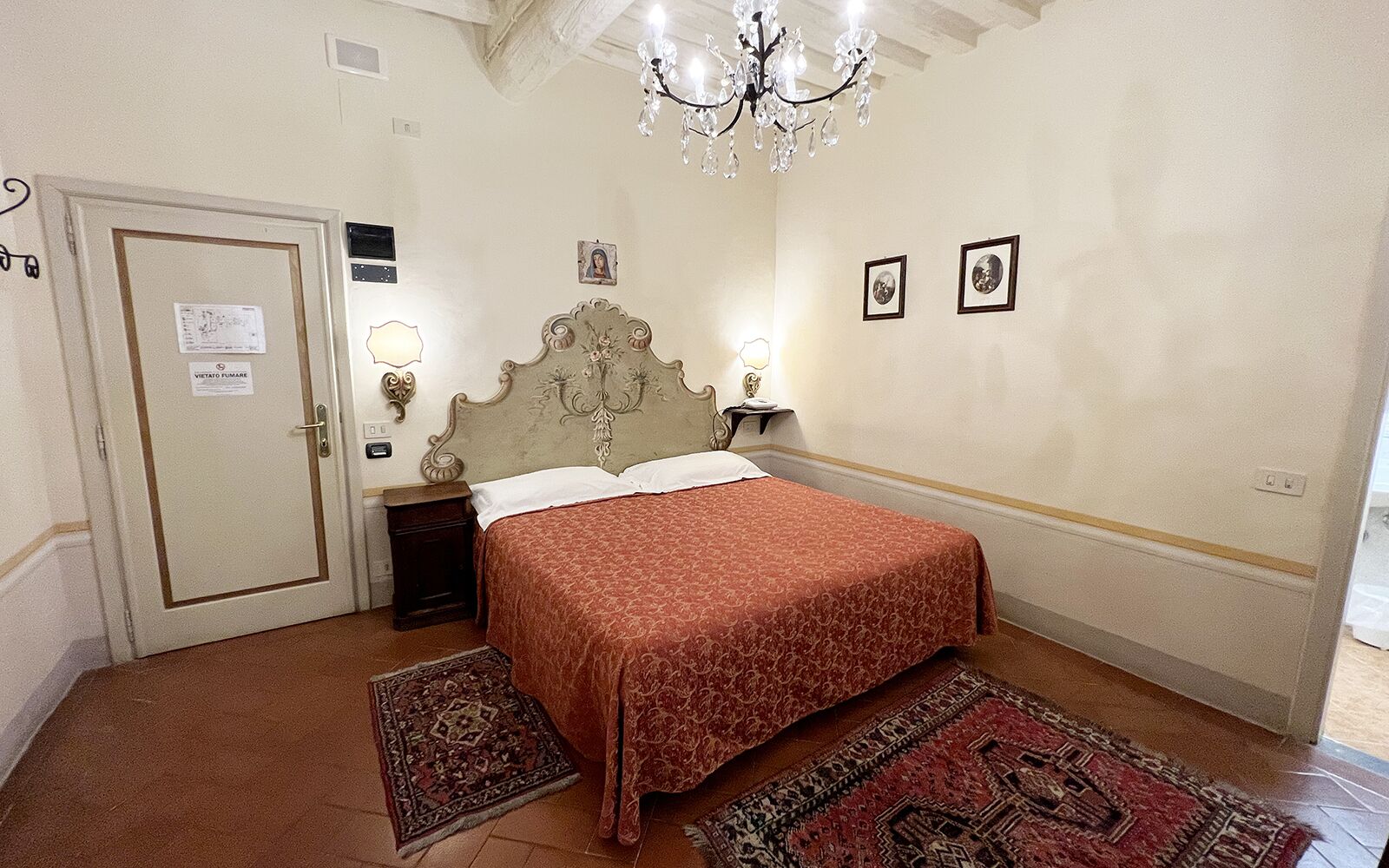 Een slaapkamer met een bed, een kroonluchter, een nachtkastje en een deur met een bordje.