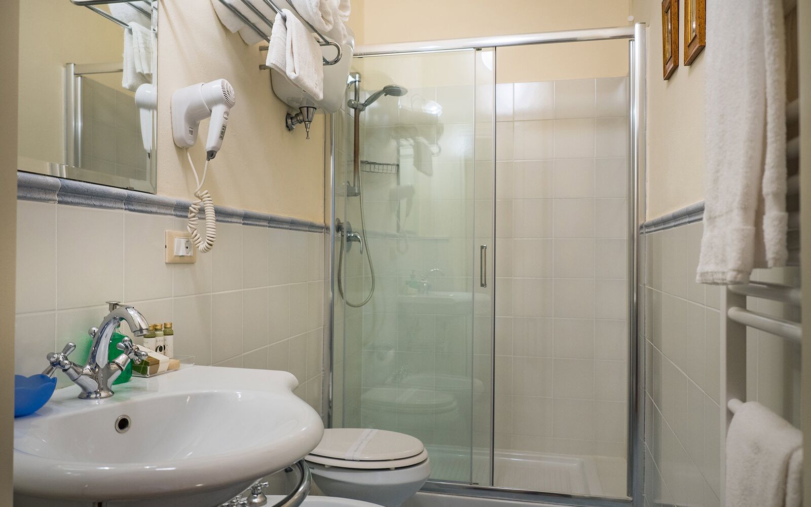 Egy fürdőszoba mosdókagylóval, WC-vel és üvegfalas zuhanykabinnel.
