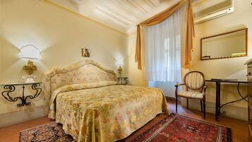 A bedroom with a floral bedspread, a wooden chair, a desk, and a mirror.