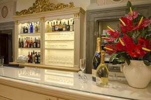 Egy bárpult, melyen sorban állnak a különböző alkoholos italok üvegei, egy pénztárgép és egy dísznövény található.