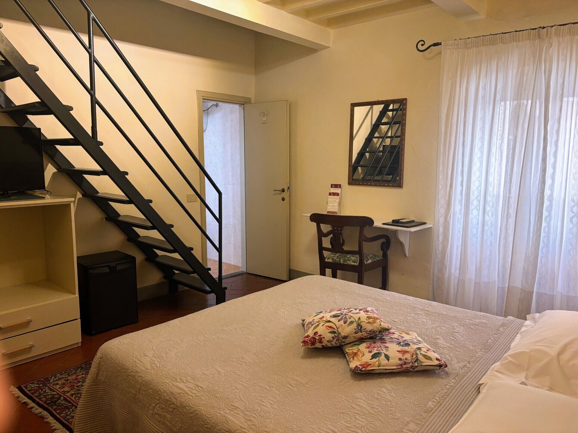 Une chambre à coucher avec un lit, des oreillers, un bureau, une chaise, un téléviseur et un escalier.