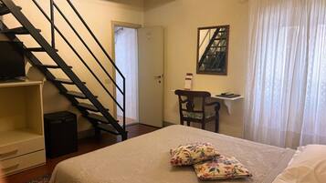 Une chambre à coucher avec un lit, des oreillers, un bureau, une chaise, un téléviseur et un escalier.