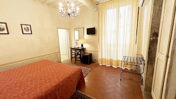 Habitación de hotel con cama, escritorio, silla, televisor y candelabro.