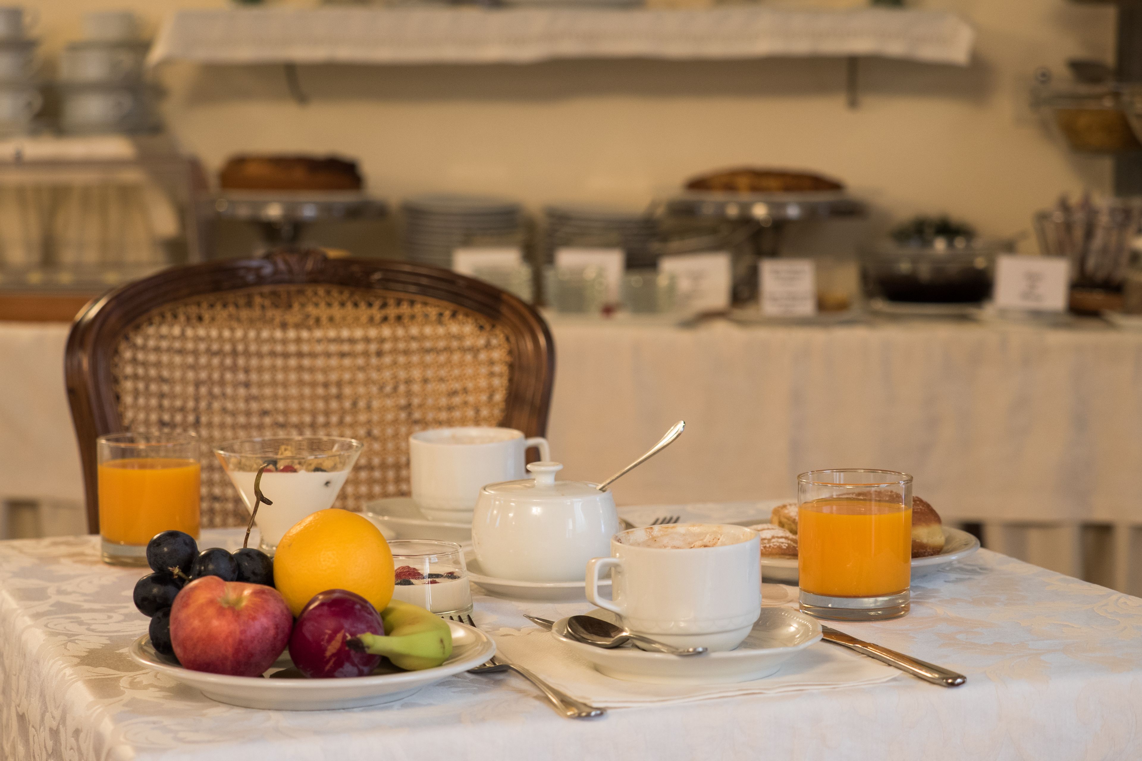 A breakfast table with fruits, a glass of orange juice, a cup of coffee, and a teapot.