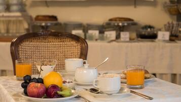 A breakfast table with fruits, a glass of orange juice, a cup of coffee, and a teapot.