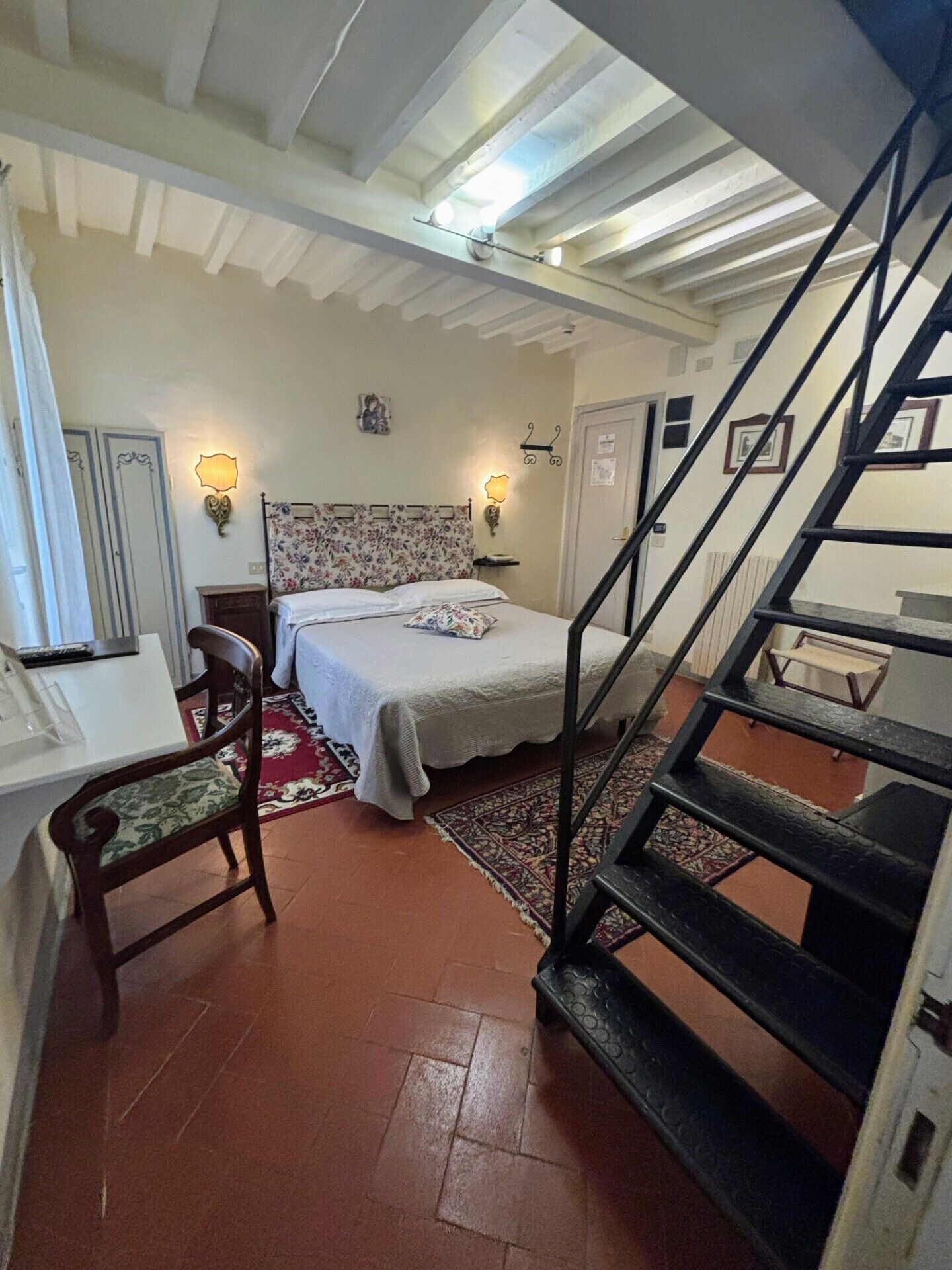 A bedroom with a bed, a chair, a desk, and a staircase.