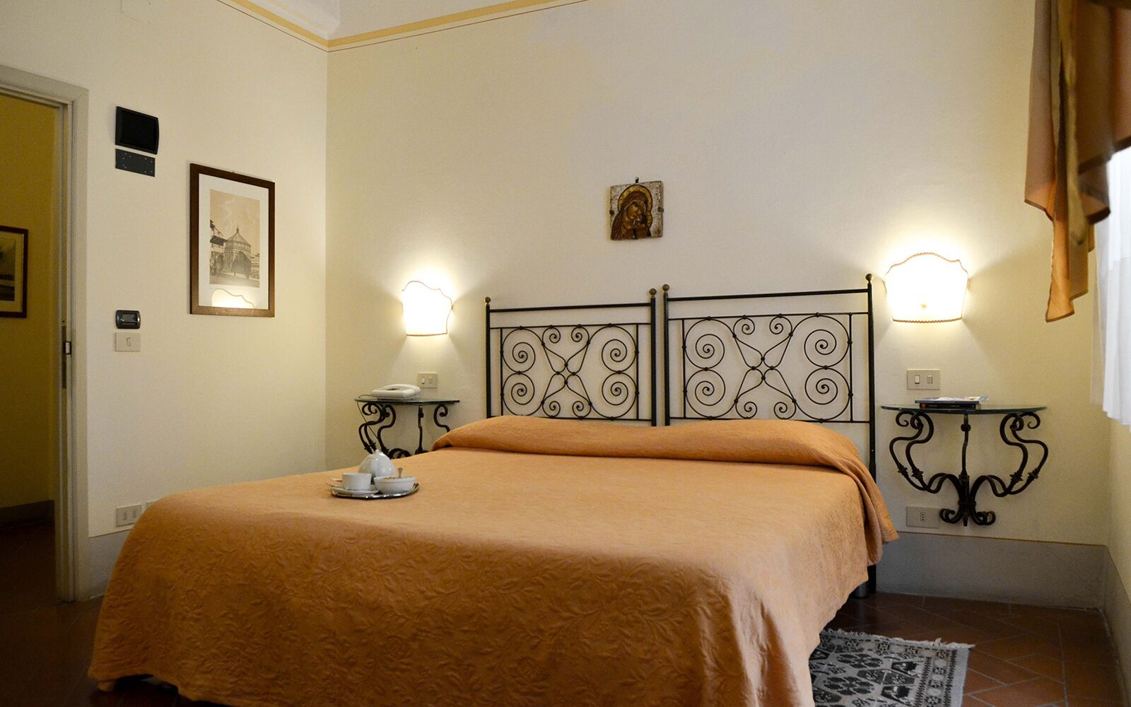 Un lit bien fait, recouvert d’une couverture marron, deux tables de chevet avec des lampes, un tableau encadré accroché au mur et un petit objet décoratif placé au-dessus de la tête de lit.