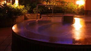 A hot tub with a wooden deck and stone walls, surrounded by plants and a wooden fence. - Yamashiro Onsen Ryokan Tatami (Kaga)
