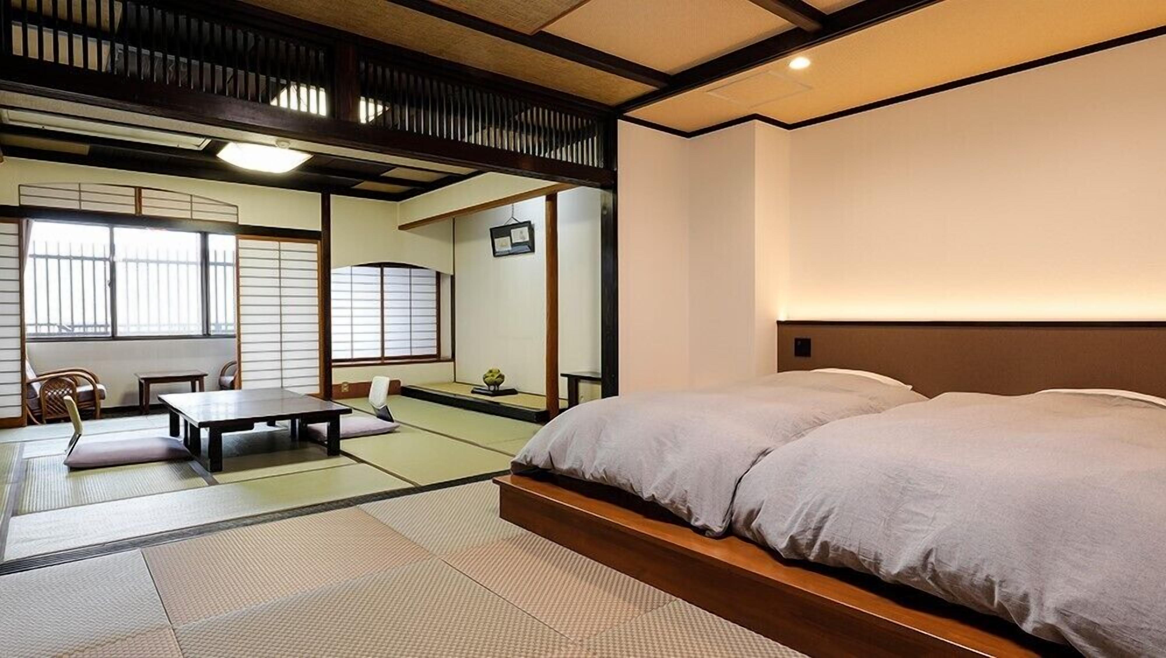 A traditional Japanese room with tatami flooring, a low wooden bed, a table, and sliding shoji doors.