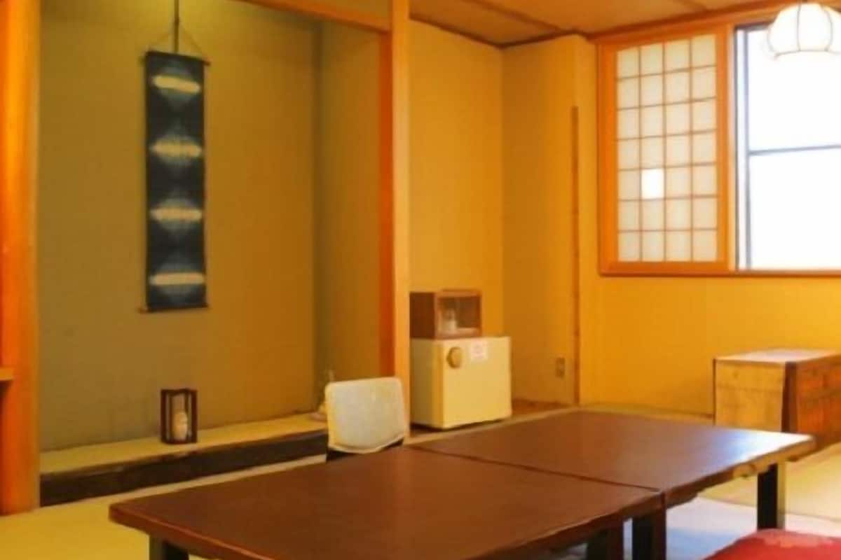 Una habitación con esteras de tatami, una mesa baja, un calentador tradicional japonés y una ventana con puertas shoji.