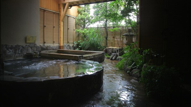 A traditional Japanese onsen with a stone bath, wooden benches, and a natural stone pathway. - Yamashiro Onsen Ryokan Tatami (Kaga)