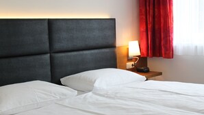 A hotel room with a large bed, a nightstand with a lamp, and a window with red curtains. - Hotel Klaus im Weinviertel (Wolkersdorf im Weinviertel)
