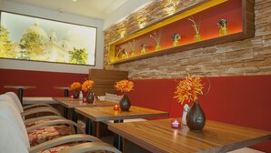 A restaurant with wooden tables and chairs, vases with flowers, and a stone wall with a shelf displaying vases. - Hotel Klaus im Weinviertel (Wolkersdorf im Weinviertel)