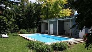 A rectangular swimming pool with a covered patio area, surrounded by a well-maintained lawn and various plants. - Hotel Klaus im Weinviertel (Wolkersdorf im Weinviertel)