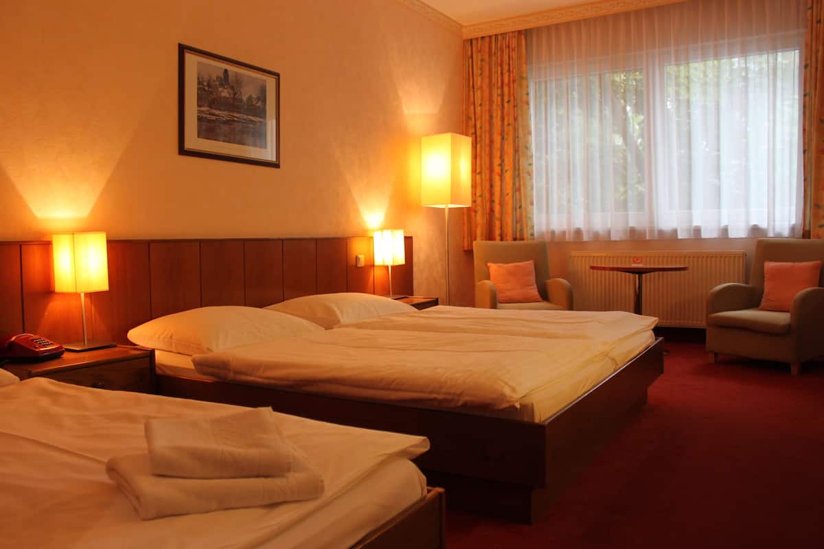 A hotel room with two beds, a sitting area with a chair and a table, and a large window with curtains.