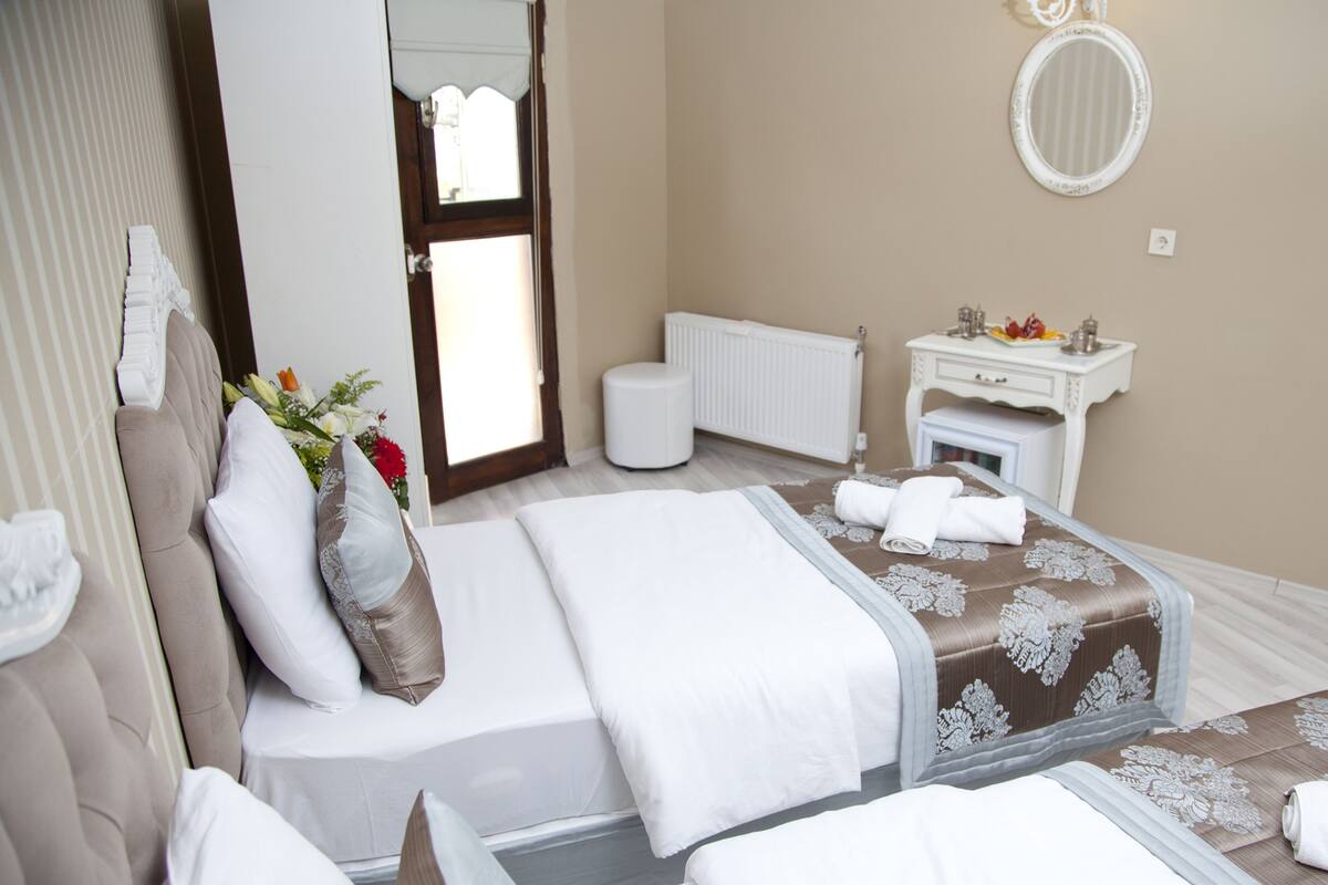 Habitación de hotel con dos camas, baño, tocador con artículos de aseo y vista a la calle.