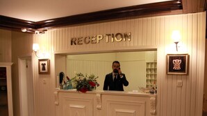 Un área de recepción con un letrero que dice 'RECEPTION', un espejo, un florero con flores y un cuadro en la pared.