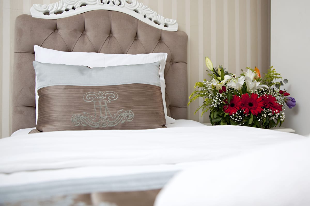 Una cama con cabecera capitonada, dos almohadas y un arreglo floral.