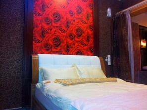 A bed with white bedding and a headboard, a patterned wall behind it, and a door to the right.