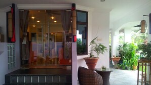 L’entrée d’un hôtel avec une porte en verre, une plante en pot, des meubles en osier et un sol carrelé.