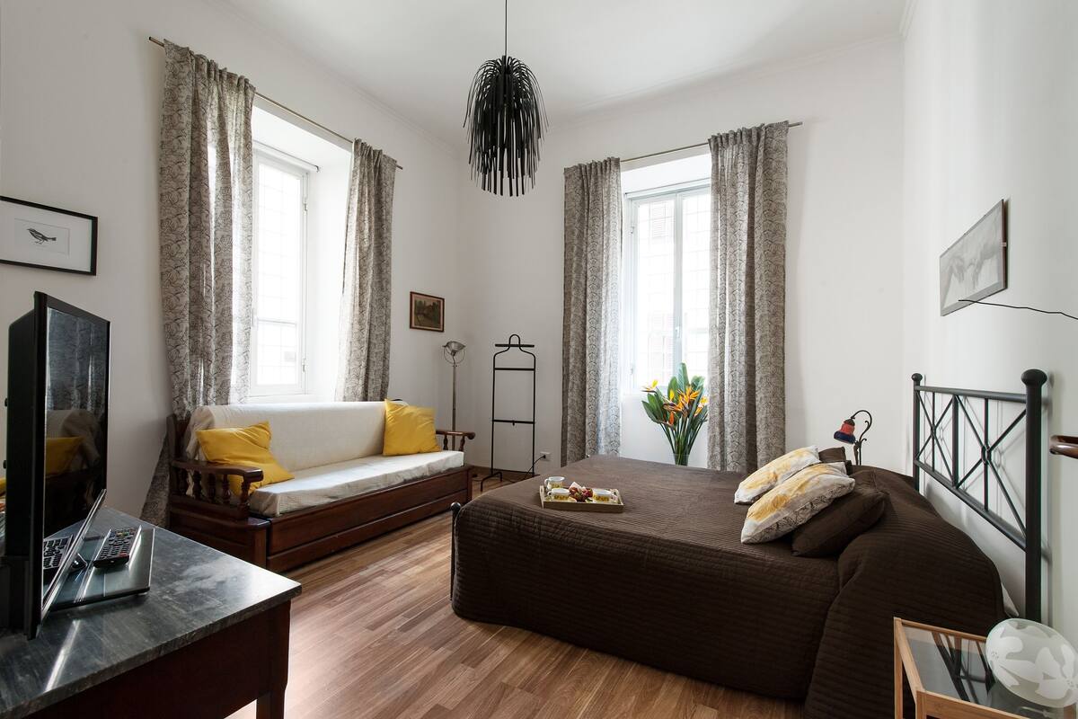 A bedroom with a bed, a sofa, a desk, and a TV.