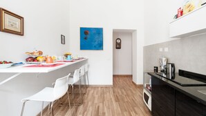 Eine moderne Küche mit weißen Arbeitsplatten, einem schwarzen Herd und Holzboden. Weiße Stühle stehen an der Bar, und an der Wand hängt ein blaues Gemälde.