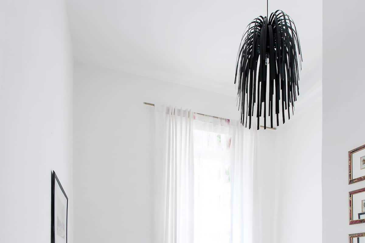 A modern bedroom with a bed, a white desk, a television, and a hanging light fixture.