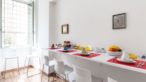 Eine moderne Küche mit weißen Barhocker, einem Esstisch mit roten Platzsets und einem Fenster mit Blick auf Gebäude.