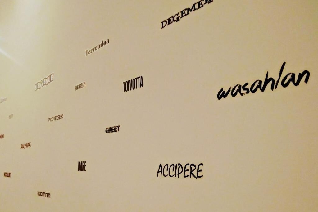 A wall with various words in different orientations and sizes, including 'TOIVOTTA' and 'ACCIPERE.'