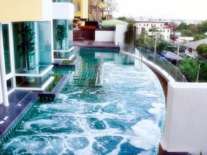 A modern hotel with a rooftop infinity pool, glass railings, and a view of the cityscape. - Impact Novo Condo Muang Thong Thani (Pak Kret)