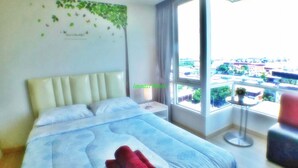 A hotel room with a large bed, a view of the city through a window, and a tree decal on the wall. - Impact Novo Condo Muang Thong Thani (Pak Kret)