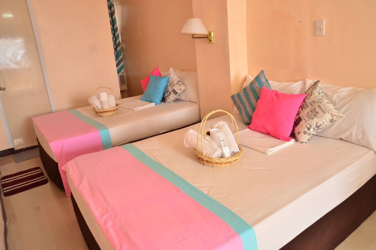Dos camas individuales con cubrecamas rosa y verde aguamarina, cada una con una cesta de toallas y almohadas.