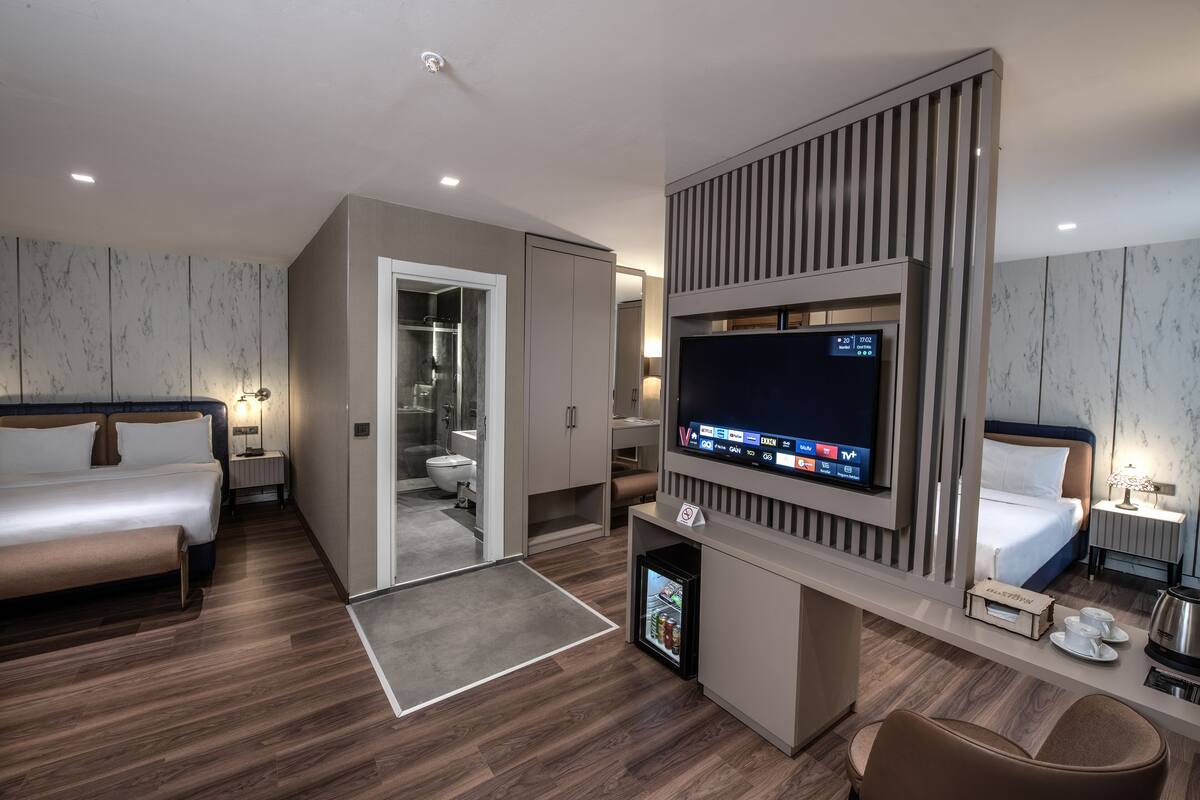 Une chambre d’hôtel moderne équipée d’un lit, d’une télévision, d’un mini-réfrigérateur, d’un bureau et d’une salle de bain.