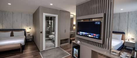 A modern hotel room with a bed, a TV, a mini-fridge, a desk, and a bathroom.