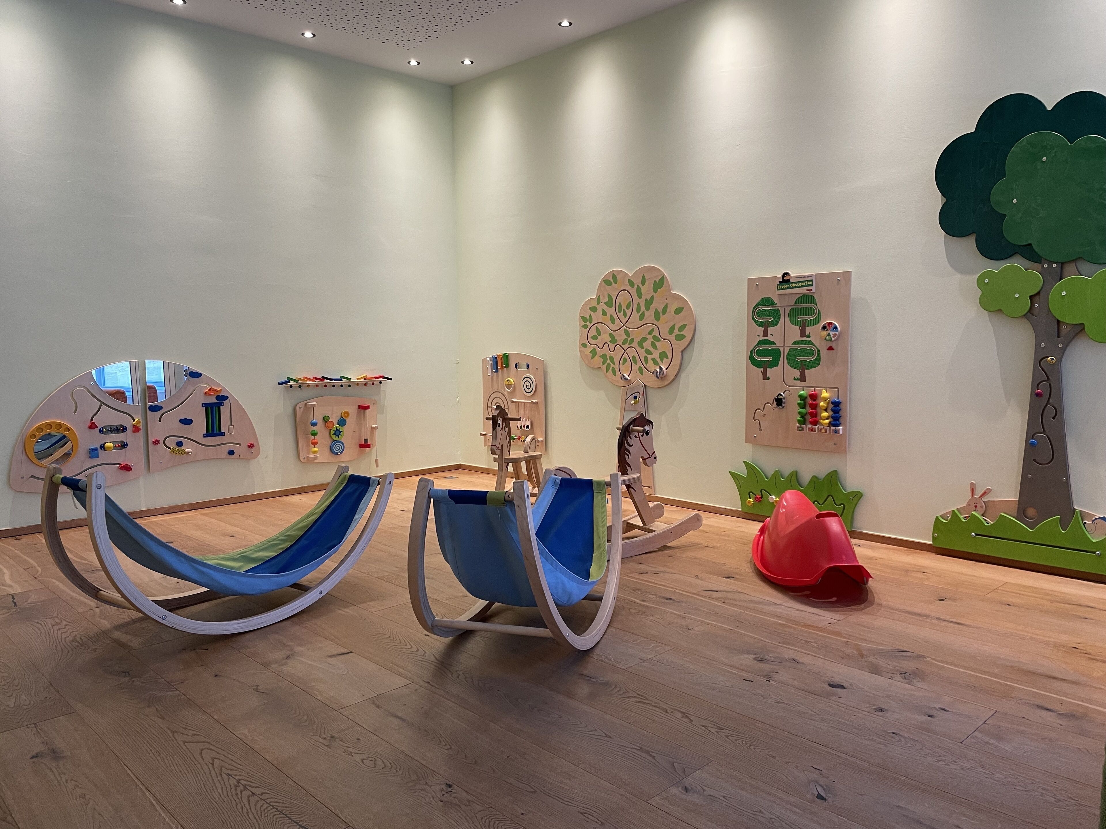 Una habitación con dos mecedoras, un espacio de juego de madera con juguetes educativos y una pared decorada con un árbol y un conejo.