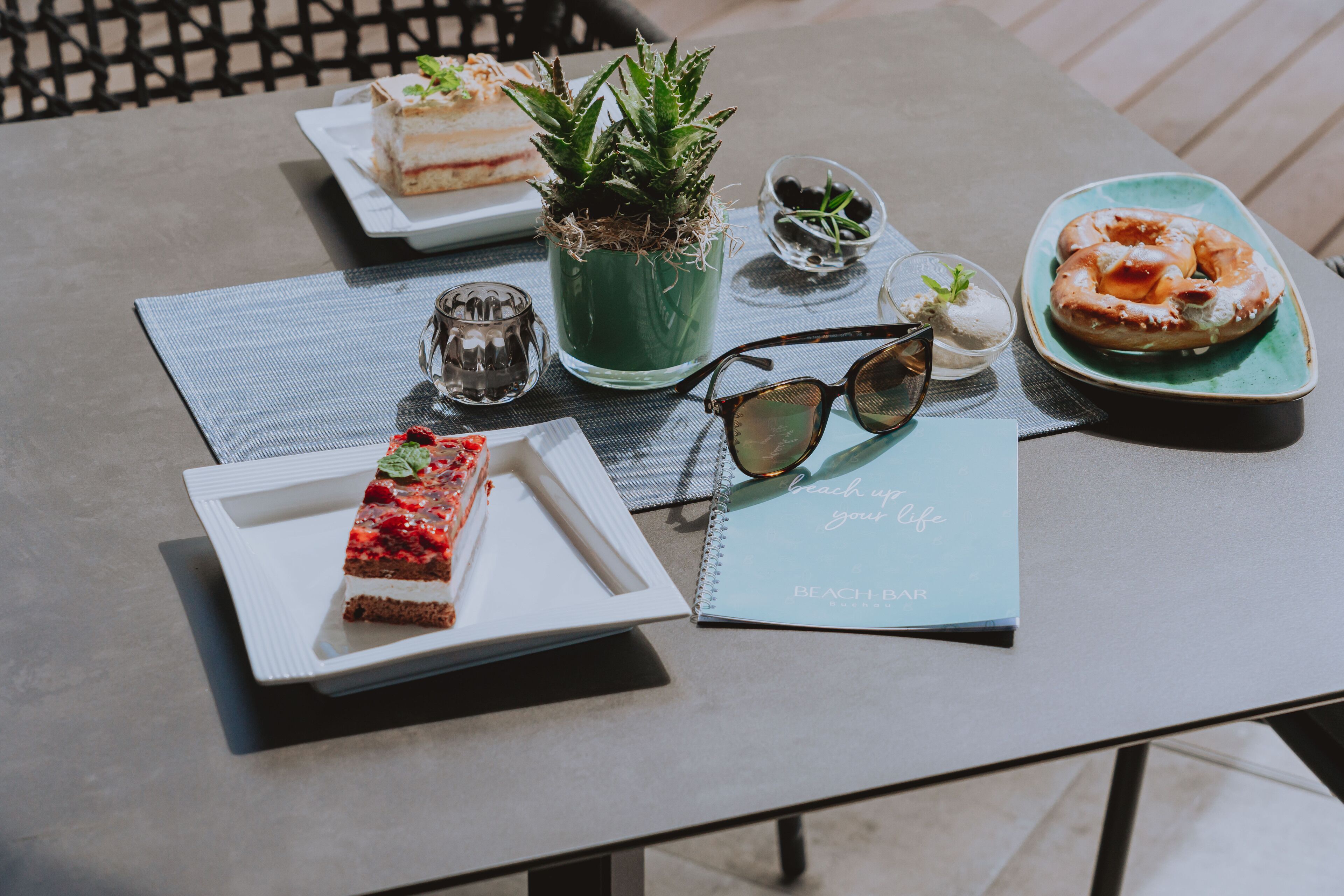 Una mesa con un cuaderno, un plato de comida, una planta y un par de gafas de sol.