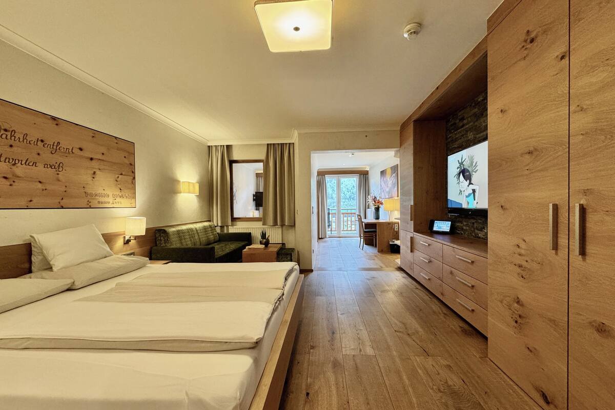 Une chambre d’hôtel avec un grand lit, une armoire en bois, une télévision et un bureau avec une chaise.