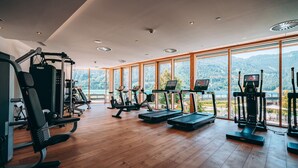 Une salle de sport équipée de machines de cardio, d’appareils de musculation et de grandes fenêtres offrant une vue sur les montagnes.