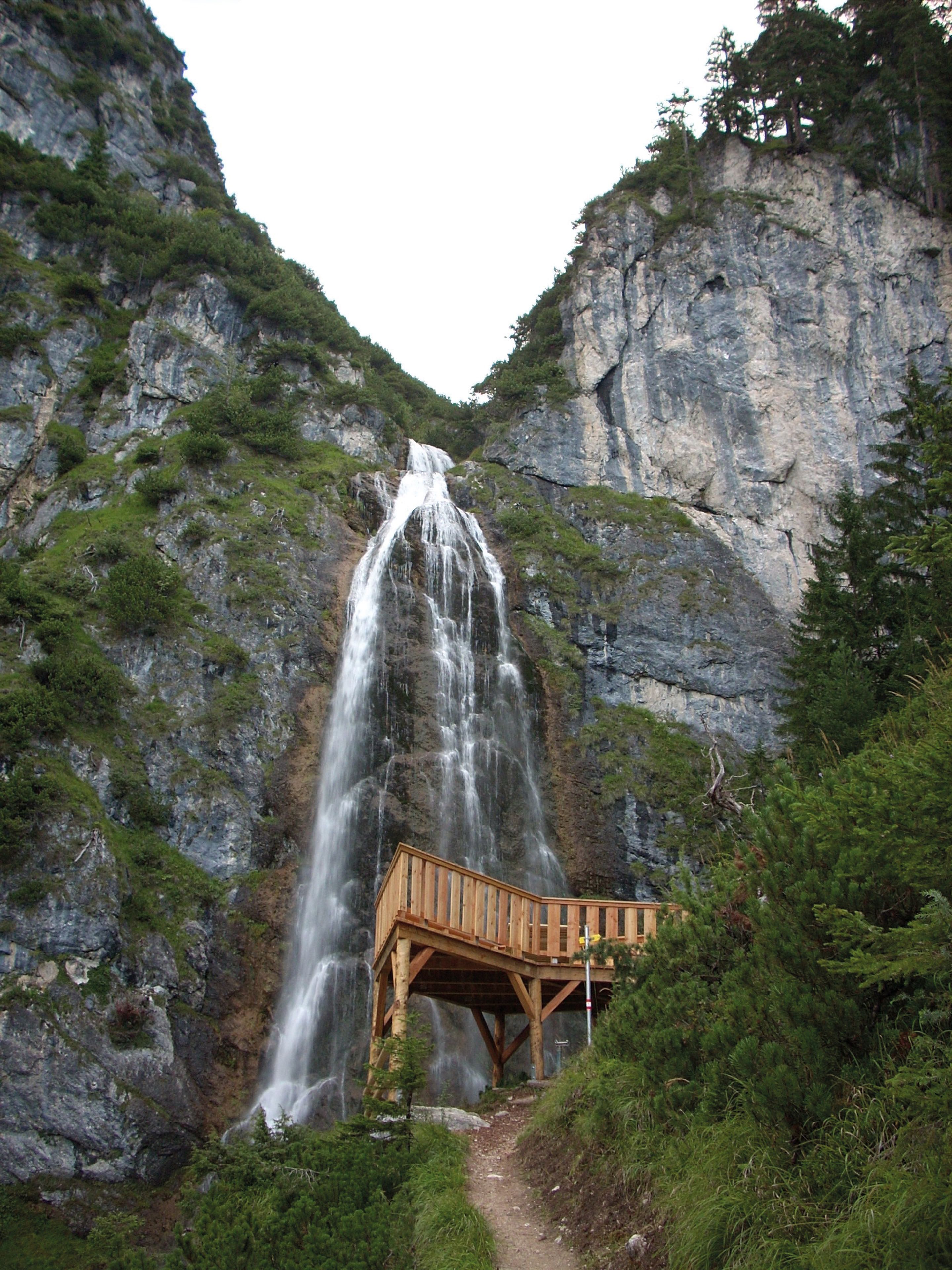 Una pasarela de madera con barandilla frente a una cascada.