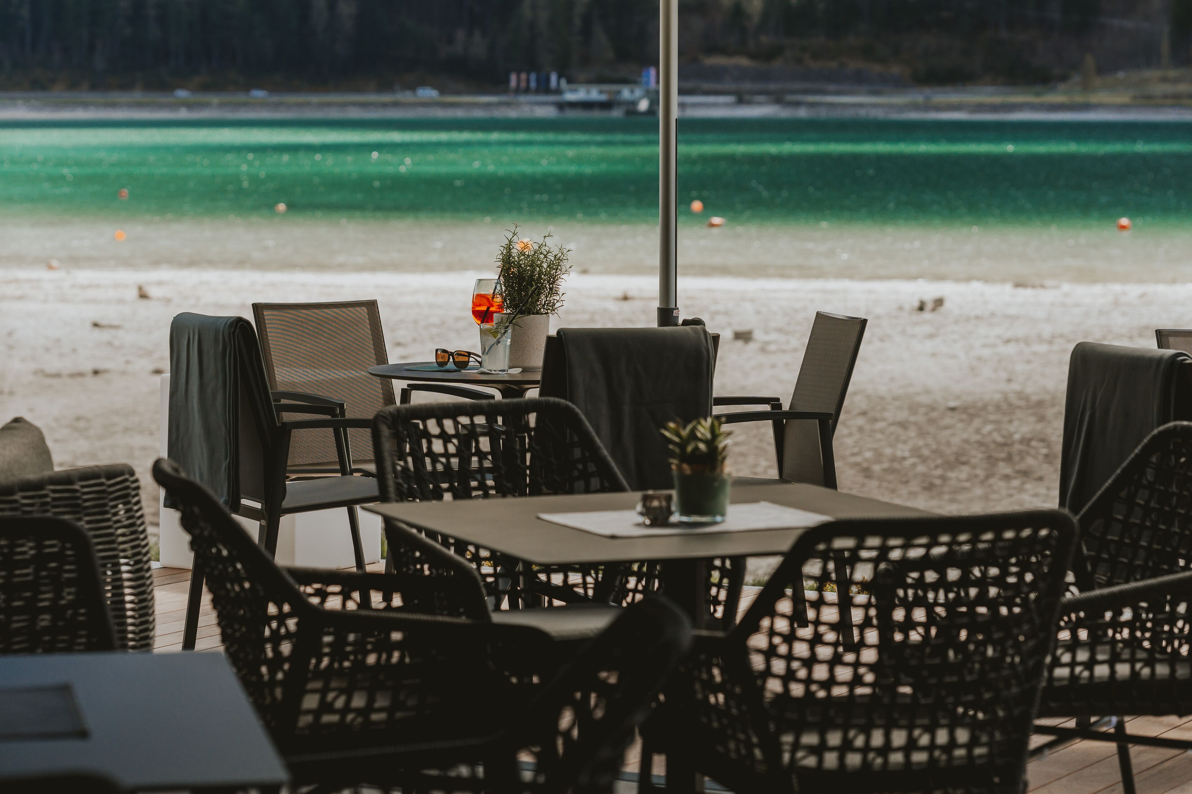 Un espace extérieur aménagé avec des chaises et des tables en osier, offrant une vue sur une plage aux eaux turquoise et cristallines.