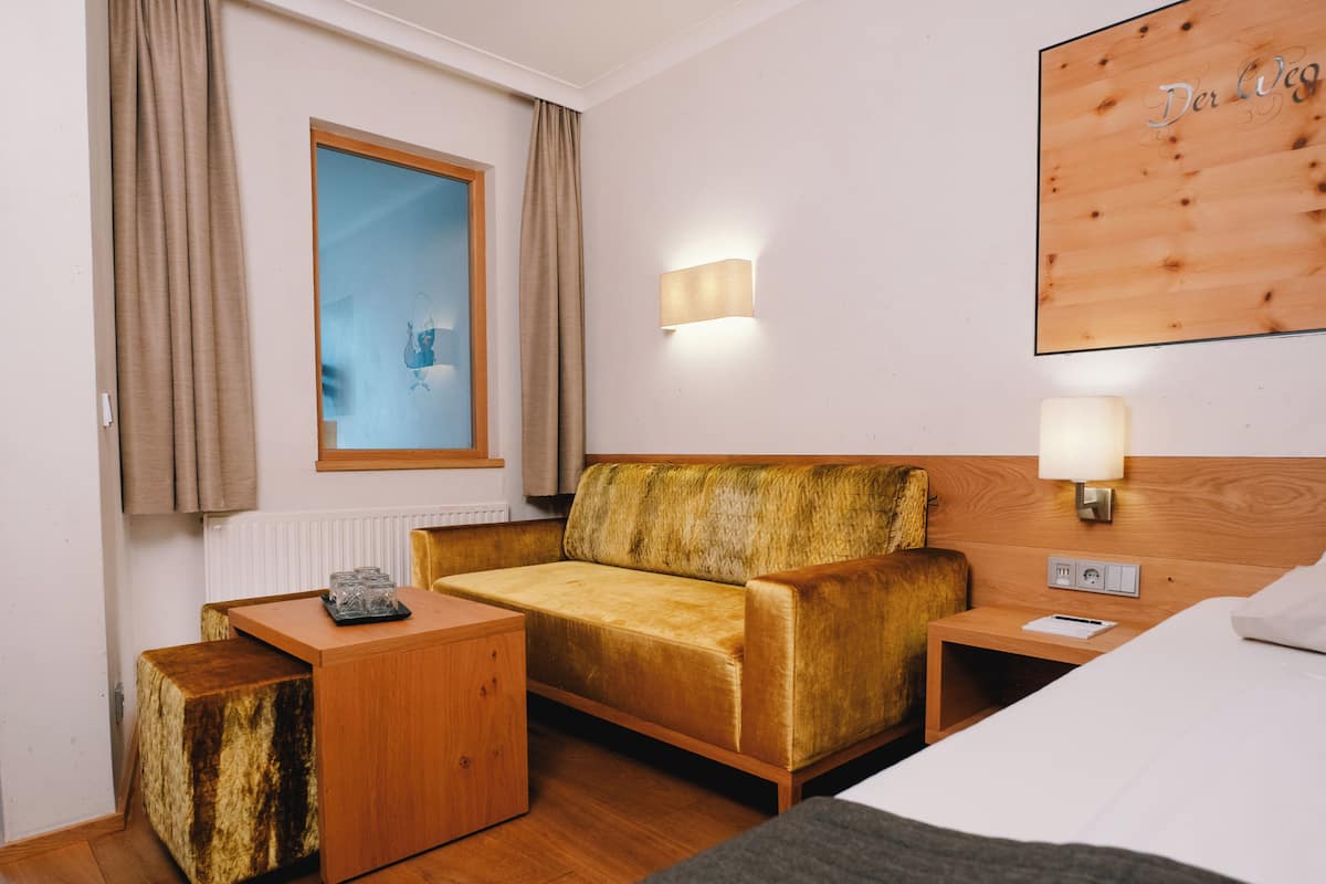Une chambre d’hôtel comprenant un lit, un canapé, une table de chevet, une petite table, une lampe, une fenêtre avec des rideaux et une œuvre d’art accrochée au mur.