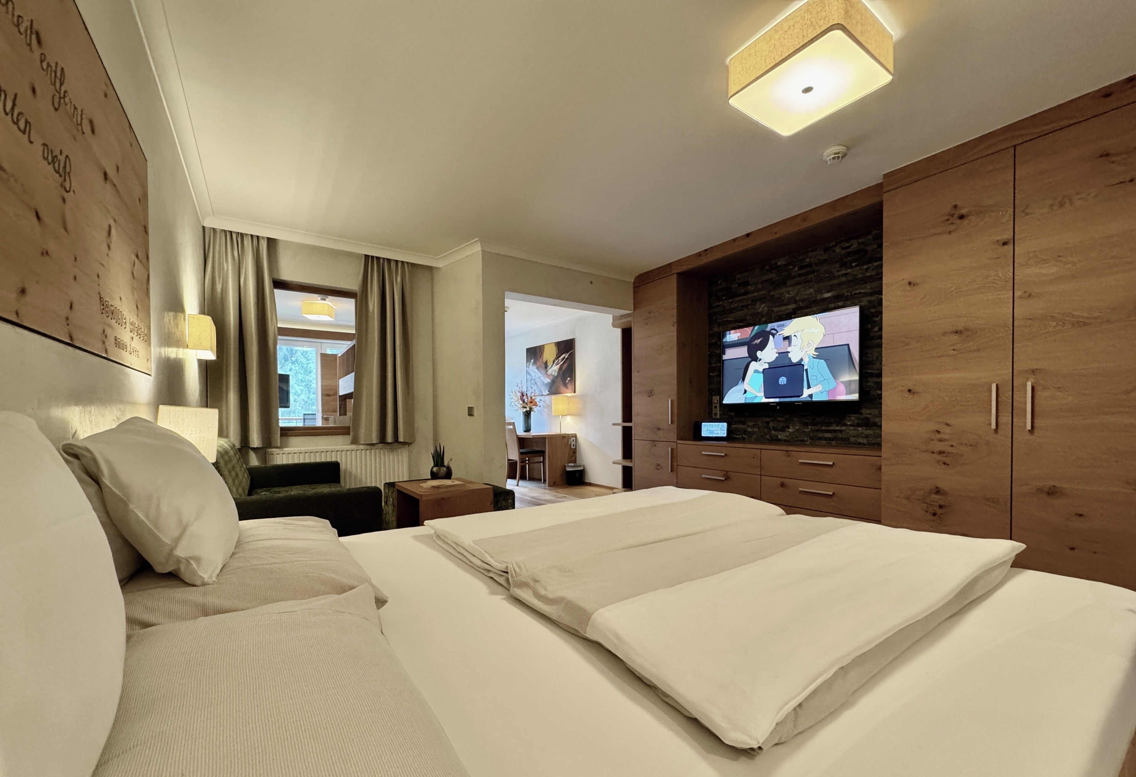 Ein Hotelzimmer mit einem großen Bett, einem Fernseher, Holzschränken und einem Schreibtisch mit Lampe.