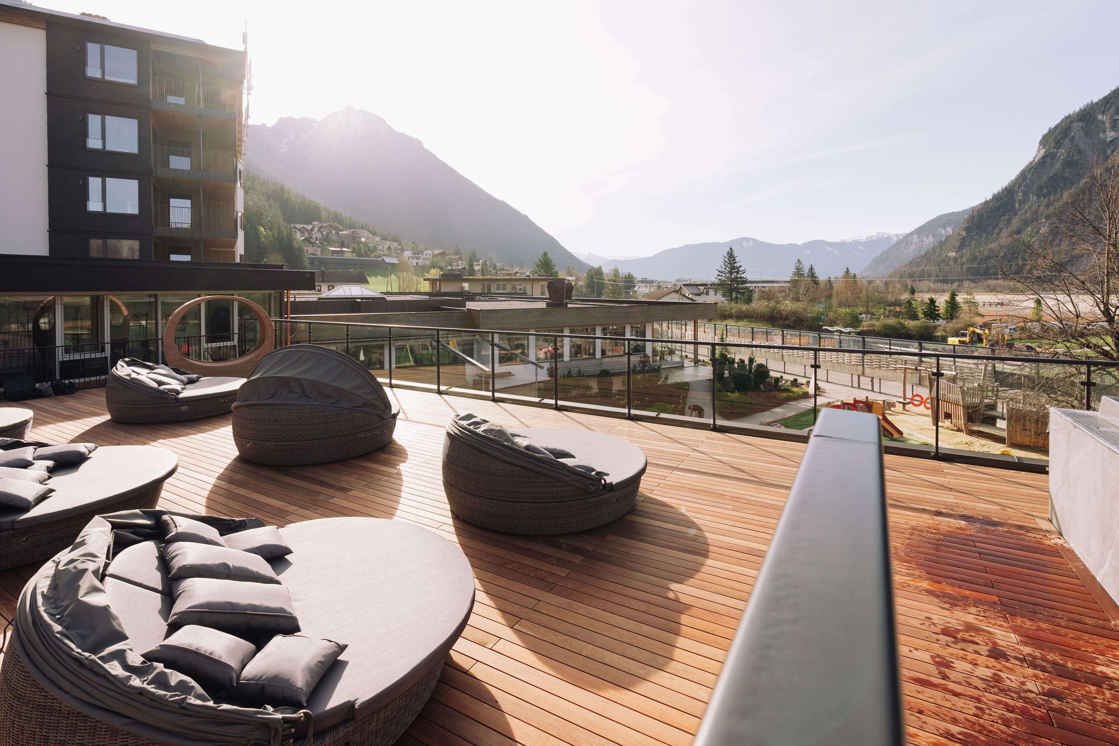 Terraço no topo do prédio com cadeiras de descanso e piscina, com vista para uma paisagem montanhosa.