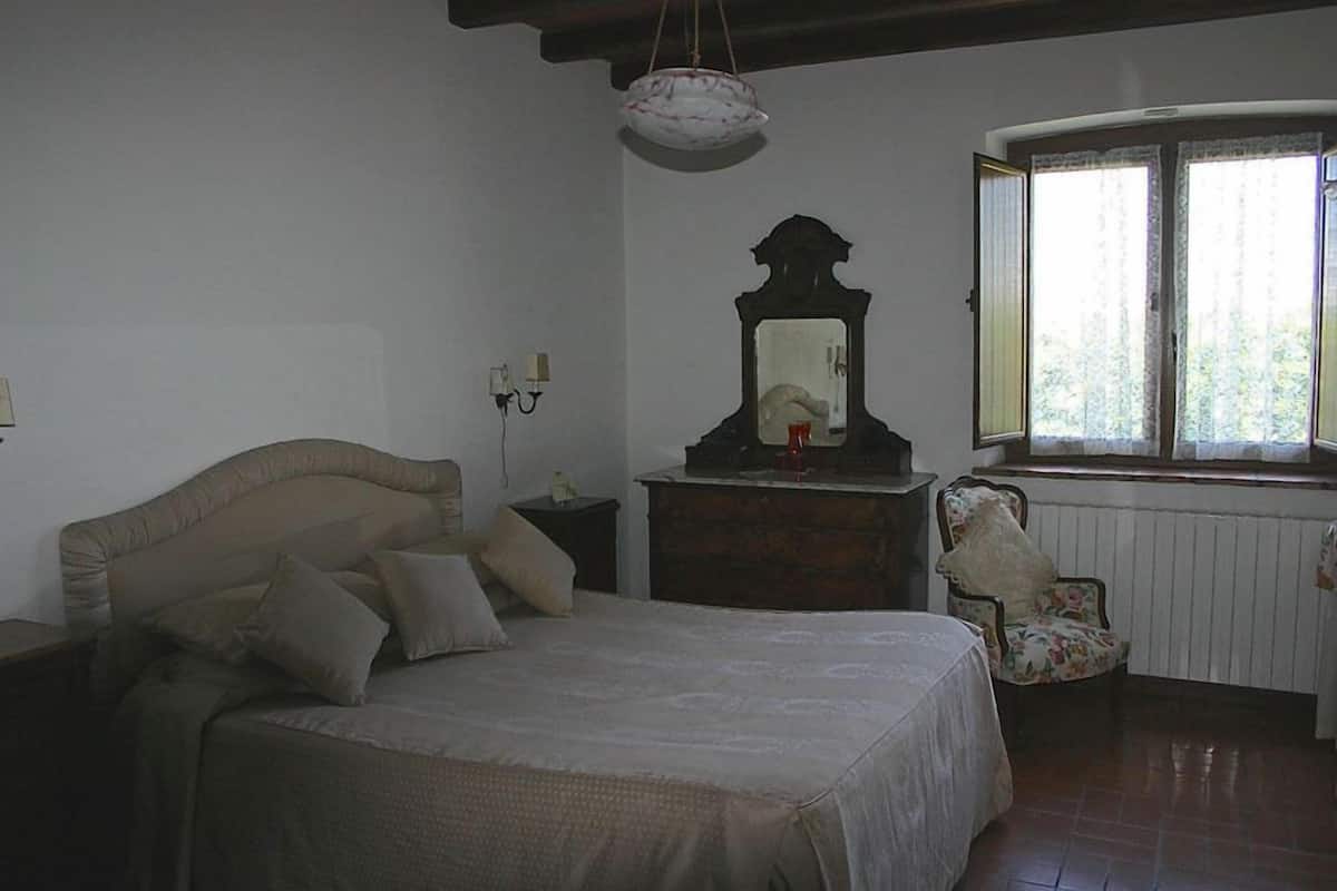 Ein Schlafzimmer mit Bett, Schminktisch, Stuhl, Spiegel und Fenster.