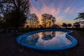 A swimming pool with a surrounding brick walkway, trees, and a gazebo in the background. - Gîte Saint-Laurent (Trois-Rivieres)